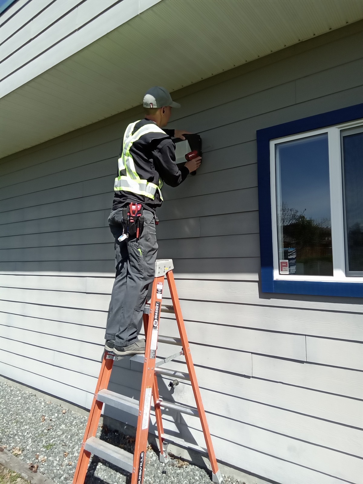 A Massey electrician replacing an exterior wall light on a ladder.