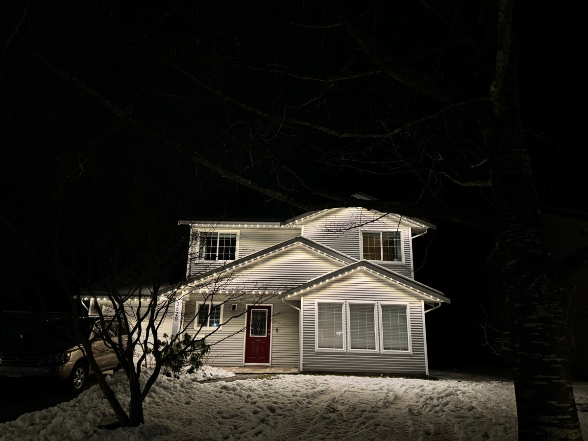 Warm white Gemstone Lights along the eaves of a two-storey home on a snowy night.