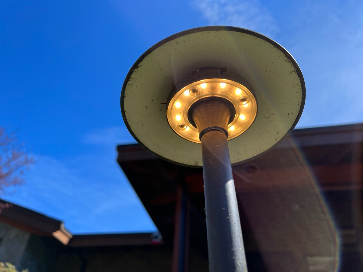 A warm LED post lamp in a garden, against a clear sky.